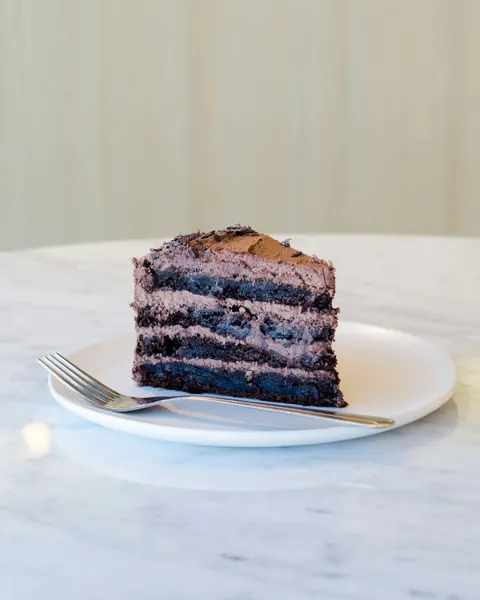 Une part de gâteau au chocolat à plusieurs couches, sur une assiette blanche