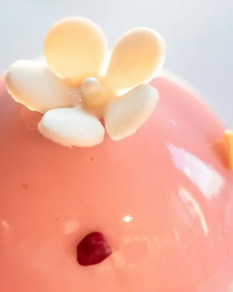 Un entremets rose au glaçage miroir, une fleur en chocolat blanc posée dessus