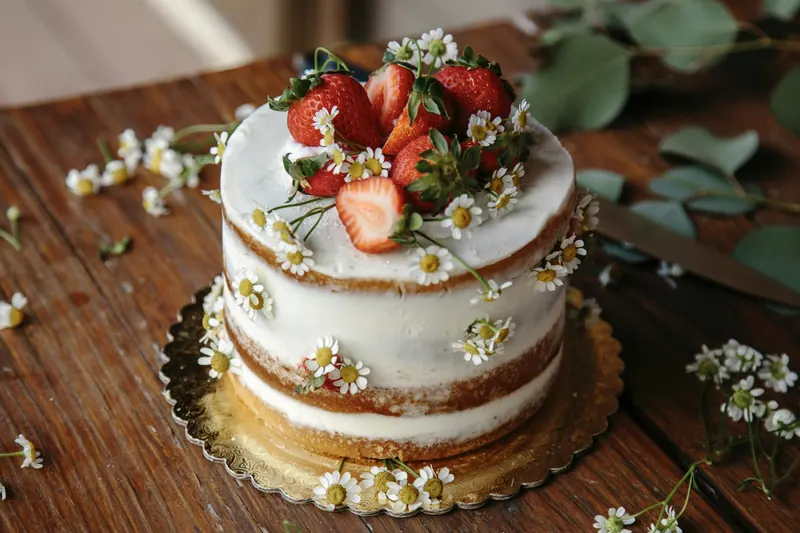 Un gâteau semi-nu couronné de fraises et de petites marguerites, sur une table en bois
